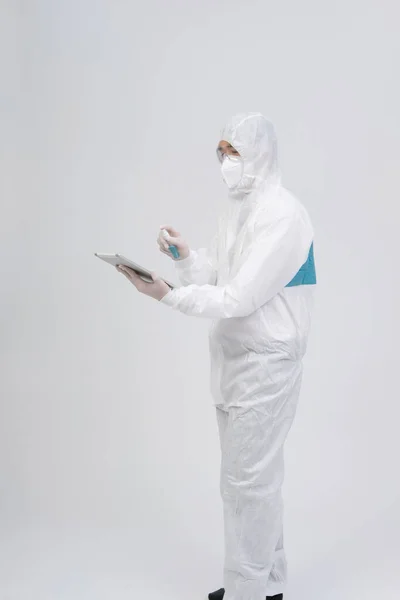 man scientist wearing biological protective uniform suit clothing, mask, gloves spraying sanitizer on tablet for sanitizing virus bacteria