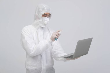 Biyolojik koruyucu kıyafet, maske, eldiven giyen bilim adamı virüs bakterilerini dezenfekte etmek için bilgisayara dezenfektan sıkıyor.