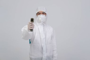 Doktor, biyolojik koruyucu üniforma, maske, vücut ısısını ölçen eldivenler ve kızılötesi alnlı termometre tabanca giyiyor.