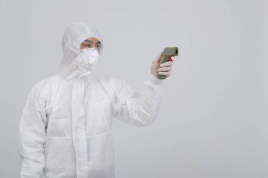 Doktor, biyolojik koruyucu üniforma, maske, vücut ısısını ölçen eldivenler ve kızılötesi alnlı termometre tabanca giyiyor.