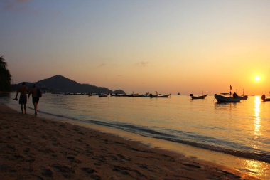 Gün batımında turistin silüet resmi plajda geziyor. .