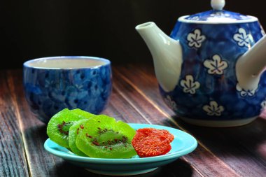 Kivi, Straberry, mavi tabakta kristalize edilmiş meyve ve siyah arka planda sıcak Çin çayı..