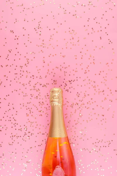 Een fles roze champagne omringd door gouden confetti sterren op — Stockfoto