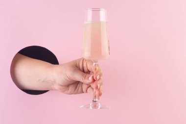 Bir bardak şampanyayı kağıt pembe poşetin içindeki delikten tutan eller.