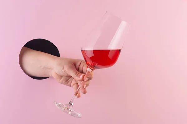 Hand holds a glass of rose wine through a hole in paper pink bac — Stock Photo, Image