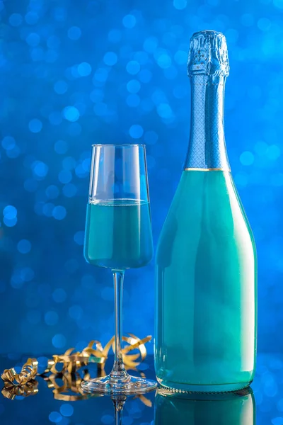 Een fles en een glas blauw gekleurde champagne tegen de achterkant — Stockfoto