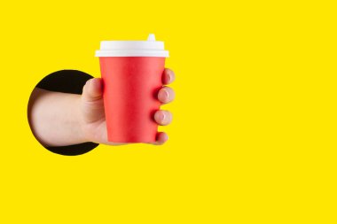 El, sarı bir deliğin içinden kahve ile kağıt bardağı tutar.