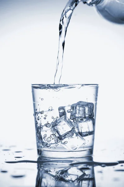 Clear mineral water is poured into a glass with ice.