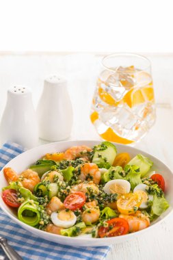 Izgara karidesli salata, taze marul, salatalık, vişneli domates ve pesto soslu bıldırcın yumurtası. Beyaz bir tabakta büyük bir porsiyon. Yemek hazır..