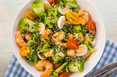 Izgara karidesli salata, taze marul, salatalık, vişneli domates ve pesto soslu bıldırcın yumurtası. Beyaz bir tabakta büyük bir porsiyon. Yemek hazır..