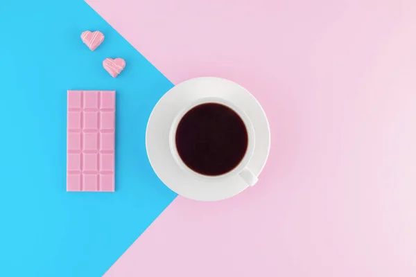 Pembe ve parlak mavi pastel arka planda bir fincan taze demlenmiş kahve. Taze tatlılar. Kremalı pasta. Pembe çikolata ve kalp şeklinde şekerler. Üst Manzara. Düz yatıyordu. 
