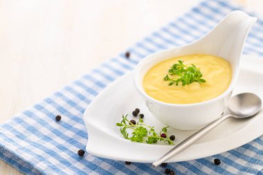 Hollandaise sosu. Klasik Fransız mutfağı sosu. Sirkeli yumurta sarısı ve tereyağı emülsiyon sosu. Mavi bir peçeteyle et suyu kabında servis edilmiş. Yakın plan.