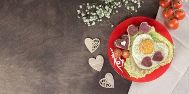 Sevgililer Günü ve Anneler Günü için lezzetli, sağlıklı bir kahvaltı. Kırmızı bir tabakta kalp şeklinde omlet, kalp şeklinde sucuklu sucuk, kalp şeklinde salam ve sosisli taze sebze. Ev yapımı yemek. Üst görünüm, pankart, düz çizgi