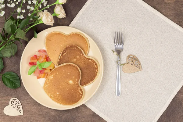 Homemade heart shaped pancakes with fruit chutney salad on a beige plate on a wooden table. Rustic style breakfast or brunch for Valentine's Day. Top view, horizontal orientation — Stock Photo, Image
