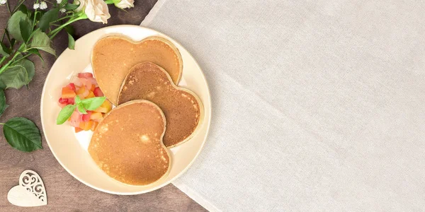 Frittelle fatte in casa a forma di cuore con insalata di chutney di frutta su un piatto beige su un tavolo di legno. Colazione o brunch in stile rustico per San Valentino. Vista dall'alto, banner, orizzontale — Foto Stock