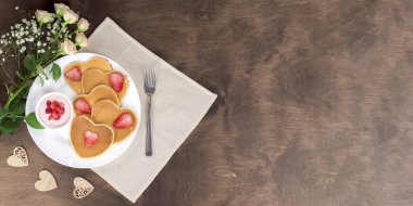 Tahta bir masada servis edilen beyaz tabakta çilek dilimleri ve çilek kremalı ev yapımı kalp şeklinde krepler. Kırsal tarzda kahvaltı ya da brunch. Üst görünüm, kopyala boşluk, afiş, yatay