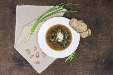 Yaban mantarlı mantar çorbası, sebze, yeşil soğan, sarımsak ve ev yapımı ekşi krema. Siyah ahşap arka planda beyaz tabakta, peçeteli geleneksel bir tabak.