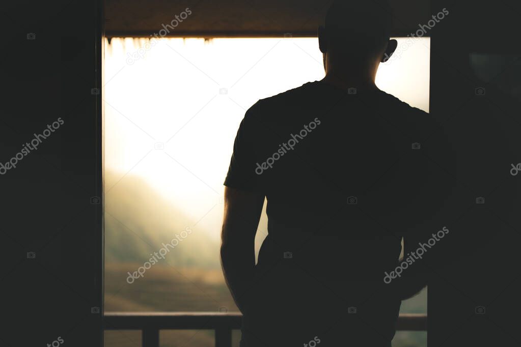 White adult male looking out through a doorway from a cabin over a beautiful mountain scene with fog and mist rolling down during sunrise