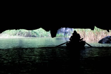 Tam Coc, Kuzey Vietnam 'daki büyük bir kireçtaşı mağarasının altından nehir turu yapan turistlerle dolu bir tekne çıkıyor.