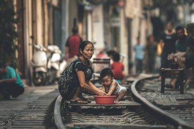 Hanoi, Vietnam - 18 Ekim 2019: Bir anne, oğlunu, Hanoi, Vietnam 'daki ünlü Tren Caddesi' ndeki tren raylarında bir küvet kullanarak halkın içinde yıkıyor.