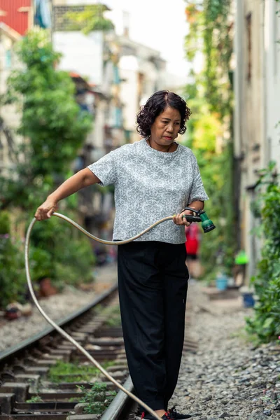 Hanoi, Vietnam - 18th October 2019: A local woman living on the world famous Train Street in Hanoi, Vietnam waters the plants and her garden — Stock Photo, Image