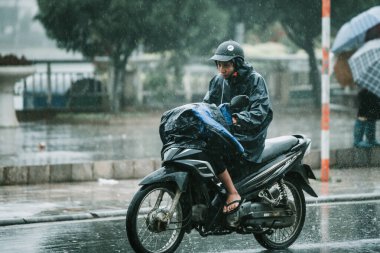 Asyalı bir erkek, kendisini korumak için üstünü örterken küçük bir dağ kasabası olan Sapa 'da sağanak yağmurda scooterını sürüyor.