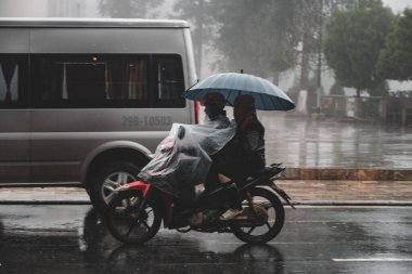 Küçük bir dağ kasabası olan Sapa, Kuzey Vietnam 'da kendilerini korumak için üzerlerini örterken, Asyalı bir kadın yağmur altında scooterına biniyor.