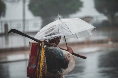 Sapa, Vietnam - 13 Ekim 2019: Şemsiye altındaki yaşlı bir Asyalı küçük Sapa kasabasındaki sağanak yağmurda kameradan uzaklaşıyor