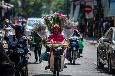 Hanoi, Vietnam - 22 Ekim 2019: Pembe giyinmiş bir kadın kurye, kapitalist Vietnam şehrinde motosiklet kullanarak çiçek getiriyor