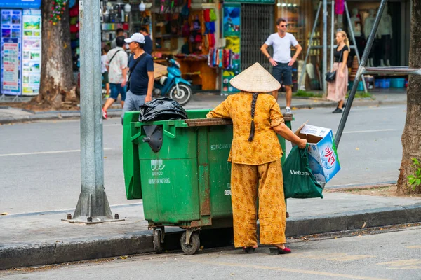 Hanoi, Vietnam - 12 de octubre de 2019: Una mujer asiática lleva basura y basura al cubo de basura verde en las calles de Hanoi, Vietnam, Asia — Foto de Stock
