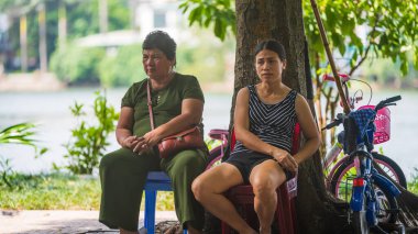 Hanoi, Vietnam - 11 Ekim 2019: İki Asyalı kadın Asya 'da sıcak hava dalgası sırasında plastik sandalyelerin altındaki bir ağacın gölgesinde oturuyor