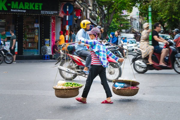 Hanoi, Vietnam - 11th October 2019: Asian woman with a wooden carrying pole transporting goods across a busy road in Hanoi, Asia — Stock Photo, Image