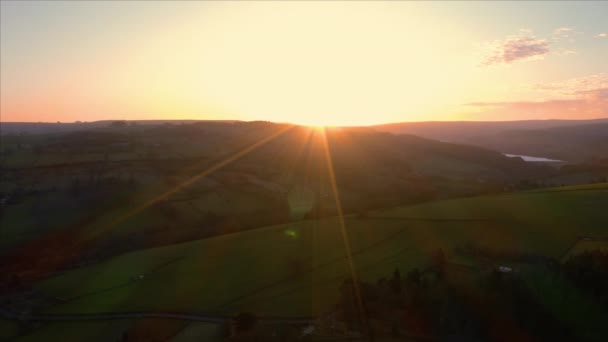Съемки с воздуха, смотрящие на солнце во время заката, пролетающие над пышными зелеными полями и лугами, полными овец и сельскохозяйственных животных в Брэдфилде, Национальный парк Пик-Дистрикт, Великобритания — стоковое видео