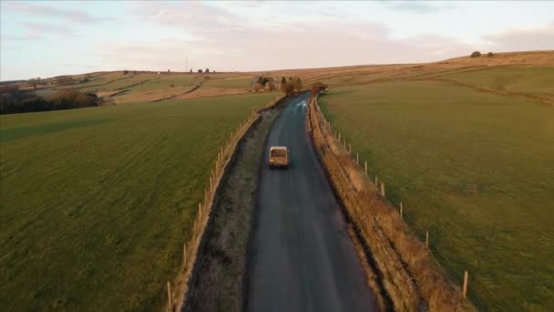 Aerial footage following a vehicle with a dog in the back as it travels across rural farm land in the English Countryside during a beautiful sunset — 비디오