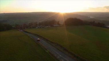Uk 'taki Peak District Ulusal Parkı' ndaki çiftlik arazisinden geçen araçların etrafında dönen hava görüntüleri, güzel bir günbatımı sırasında, 2019 Kış.