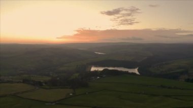 Güzel turuncu bir günbatımında Peak District Ulusal Parkı 'ndaki yeşil tarlalar, çayırlar ve çimenli tepeler üzerinde uçan hava görüntüleri.