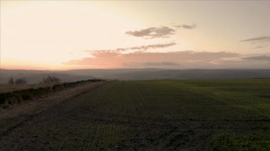 Güzel turuncu bir gün batımı sırasında Peak District Ulusal Parkı 'ndaki tepelerin olduğu ekilmiş ekili tarlaların üzerinden alçak uçan hava görüntüleri.