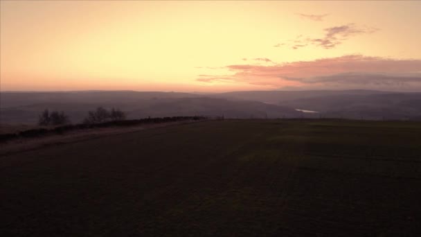 Aerial footage rotating low over rows of planted seeded farmland fields with a reveal of hills in the Peak District National Park during a beautiful orange sunset — 비디오