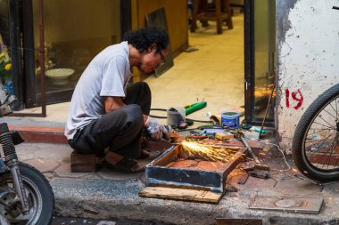 Hanoi, Vietnam - 18 Ekim 2019: Yaşlı bir Asyalı sokakta herhangi bir güvenlik giysisi veya gözlüğü olmadan bazı metalleri tamir ediyor