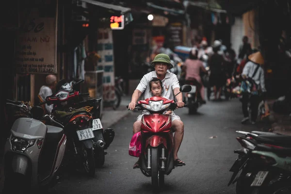 Hanoi, Vietnam - 18th October 2019: An old man rides a scooter through the back streets of Vietnam with a small girl on the front — Stock Photo, Image