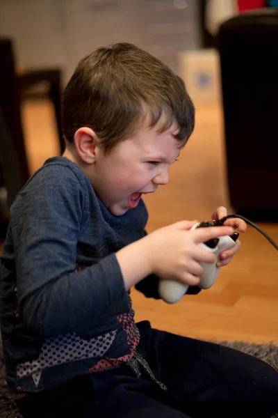 Μικρό αγόρι που παίζει ηλεκτρονικά παιχνίδια ψυχαγωγίας κονσόλα με ένα λευκό χειριστήριο στο εσωτερικό — Φωτογραφία Αρχείου