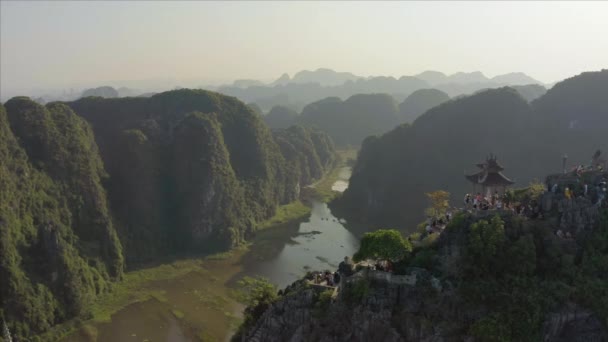 観光客は北ベトナムのニンビン省の美しい夕日の間に有名な嘘龍山の像を登る — ストック動画