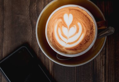 Kahve kültürünü veya milenyumların hafta sonu yaşam tarzını gösteren bir Latte ve cep telefonunun en üstteki resmi
