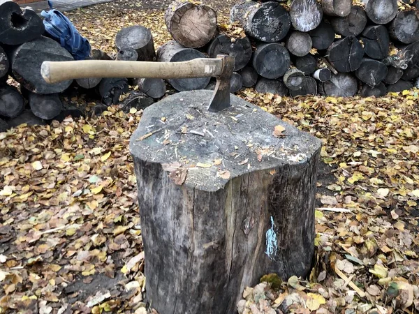 Un ceppo con un'ascia, sullo sfondo di legna da ardere. Ax con manico in legno su ceppo. Raccolta legna da ardere per l'inverno . — Foto Stock
