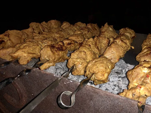 Cozinhar churrasco na grelha. Carvão queimado na grelha, churrasco com carne em espetos. Piquenique na natureza, frango cozinhado em uma fogueira, fumaça de um fogo. Pedaços de porco frito em um fundo escuro — Fotografia de Stock