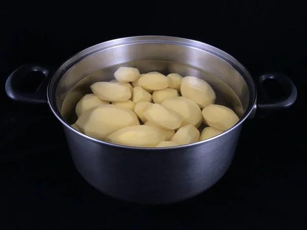 Geschilde aardappelen in een pan met water. Witte aardappelen om te koken. Vaatwerk met geschilde aardappelen, op een zwarte achtergrond. — Stockfoto