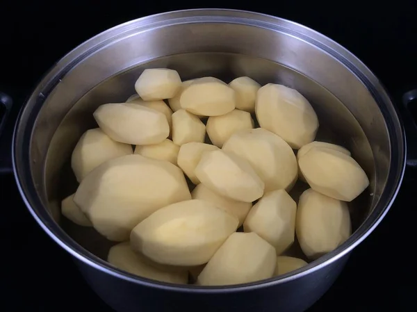 Oloupané brambory v pánvi s vodou. Bílé brambory na vaření. Nádobí s oloupanými brambory, na černém pozadí. — Stock fotografie
