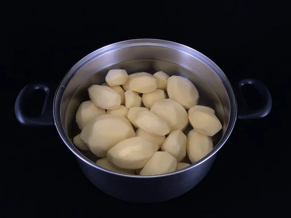 Geschilde aardappelen in een pan met water. Witte aardappelen om te koken. Vaatwerk met geschilde aardappelen, op een zwarte achtergrond. — Stockfoto