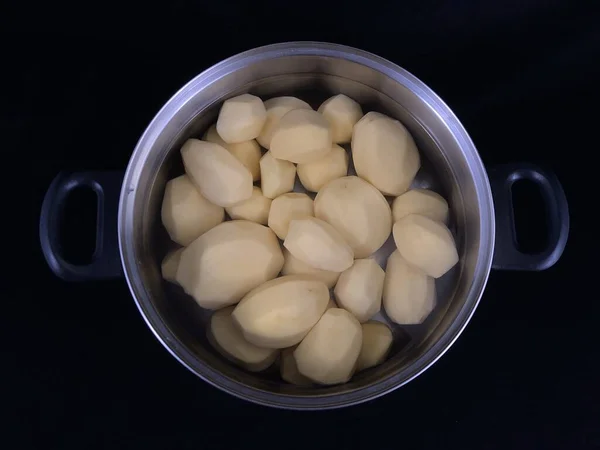 Geschilde aardappelen in een pan met water. Witte aardappelen om te koken. Vaatwerk met geschilde aardappelen, op een zwarte achtergrond. — Stockfoto