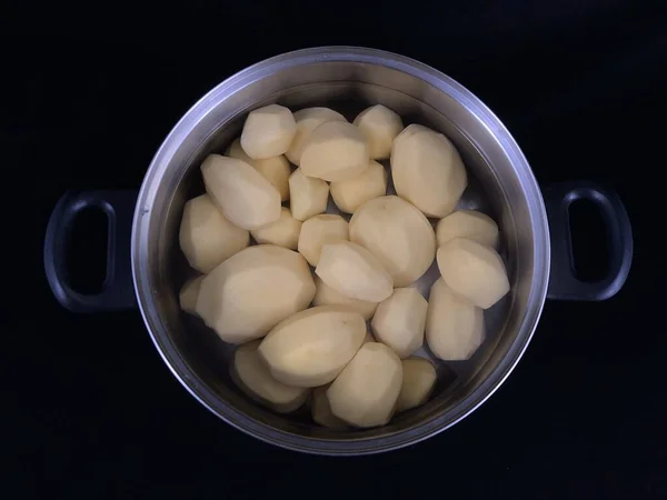 Skalad potatis i en kastrull med vatten. Vitpotatis för matlagning. porslin med skalad potatis, på en svart bakgrund. — Stockfoto